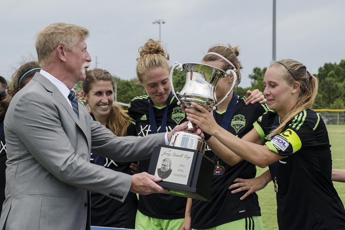 Seattle Sounders Women captain Jenna Holtz, right, receives the Jerry Zanelli Cup from WPSL Commissioner Rich Sparling, left, after her club won the 2018 WPSL Championship. | Theresa Bragg, WPSL