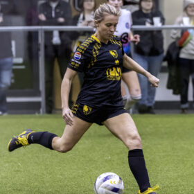Blonde soccer player kicks ball during game